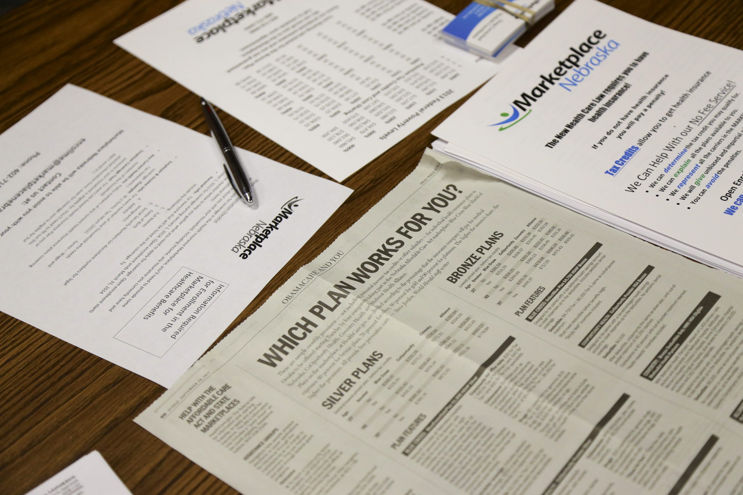 Forms and a newspaper article are spread on a table as a representative of Marketplace Nebraska, a health insurance broker under the new Affordable Care Act, explains the health insurance enrollment process and the options that are available. (AP Photo/Nati Harnik)