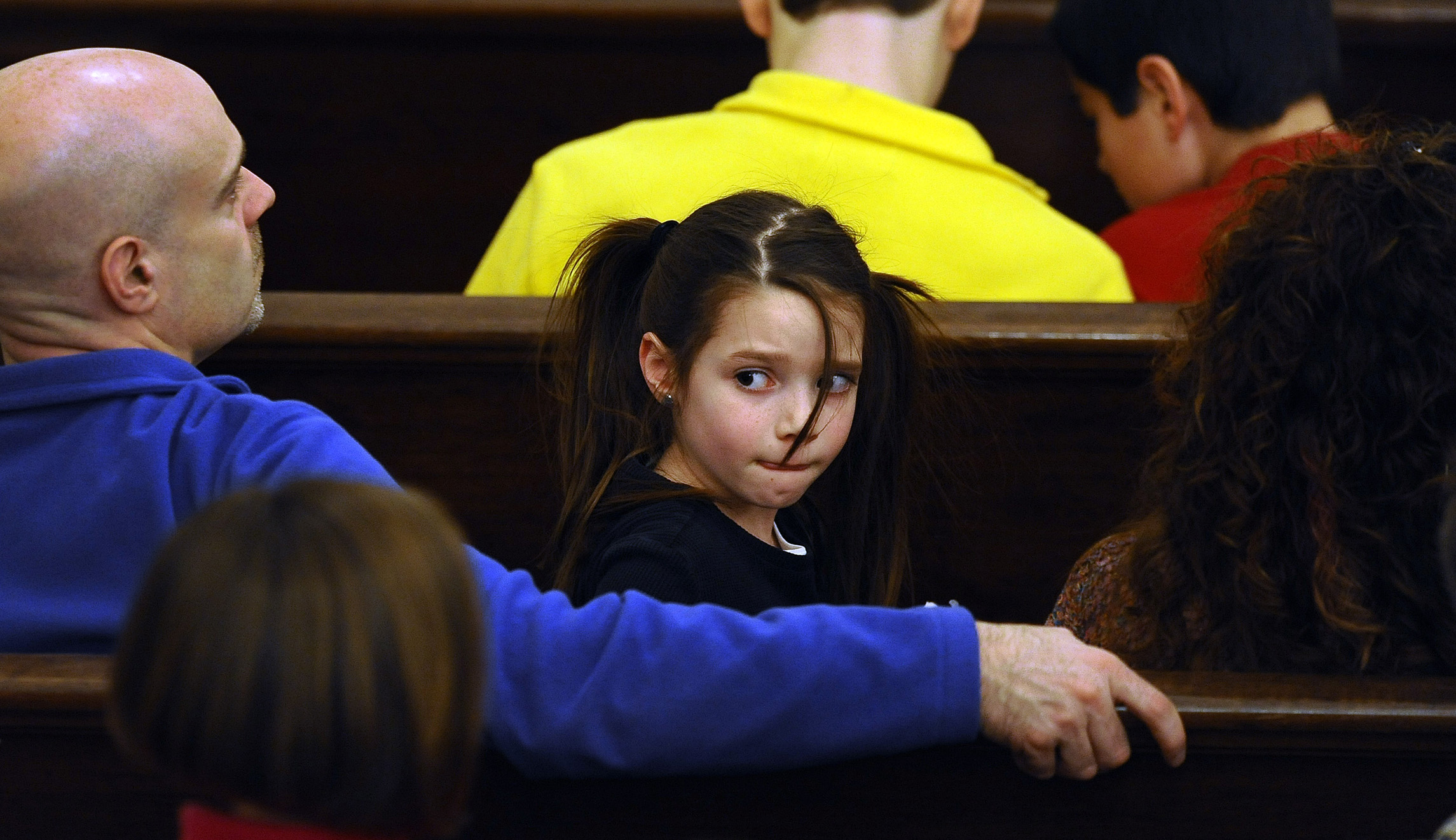 A girl sits with her family in a pew during a sermon at a church.