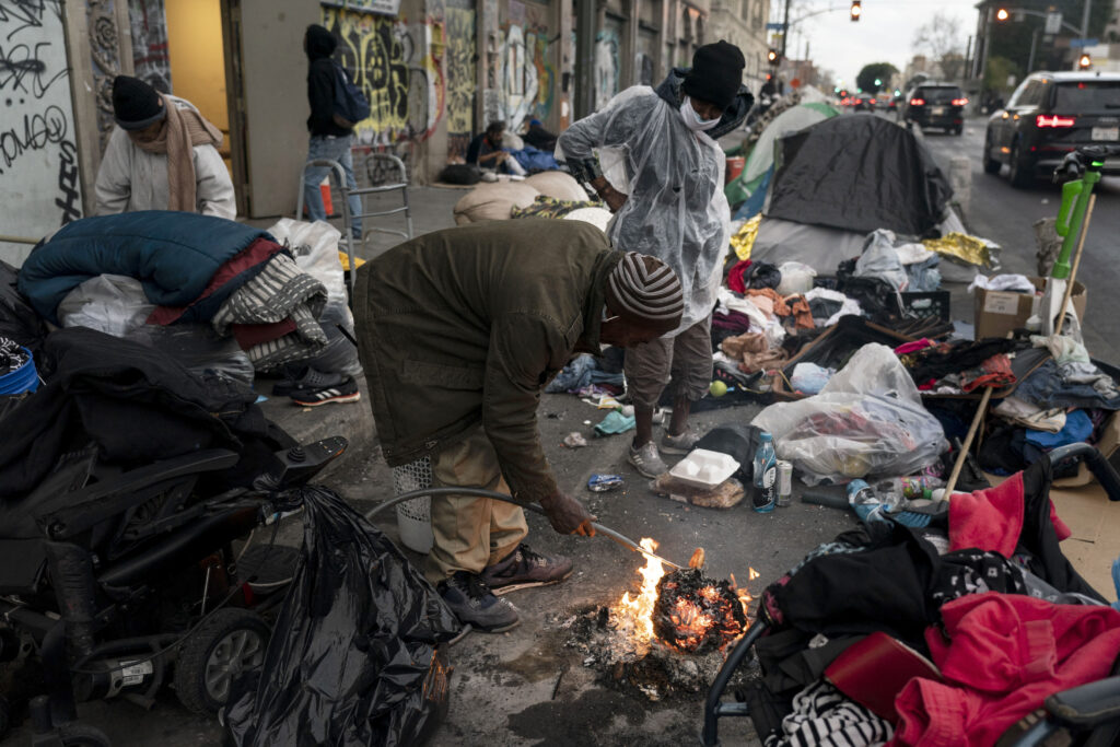 Robert Mason, a 56-year-old homeless man, warms up a piece of doughnut over a bonfire he set to keep himself warm on Skid Row in Los Angeles, on Feb. 14, 2023. Homeless people in California are already a vulnerable group, often struggling with poor health, trauma and deep poverty before they lose their housing, according to a new study on adult homelessness released Tuesday, June 20, by the University of California, San Francisco, aimed at capturing a comprehensive picture of how people become homeless in California.